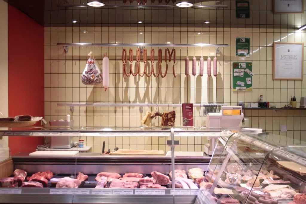 Comptoir de la Metzlerei Lucien Saeul avec saucissons et charcuterie maison suspendus au-dessus de la vitrine réfrigérée