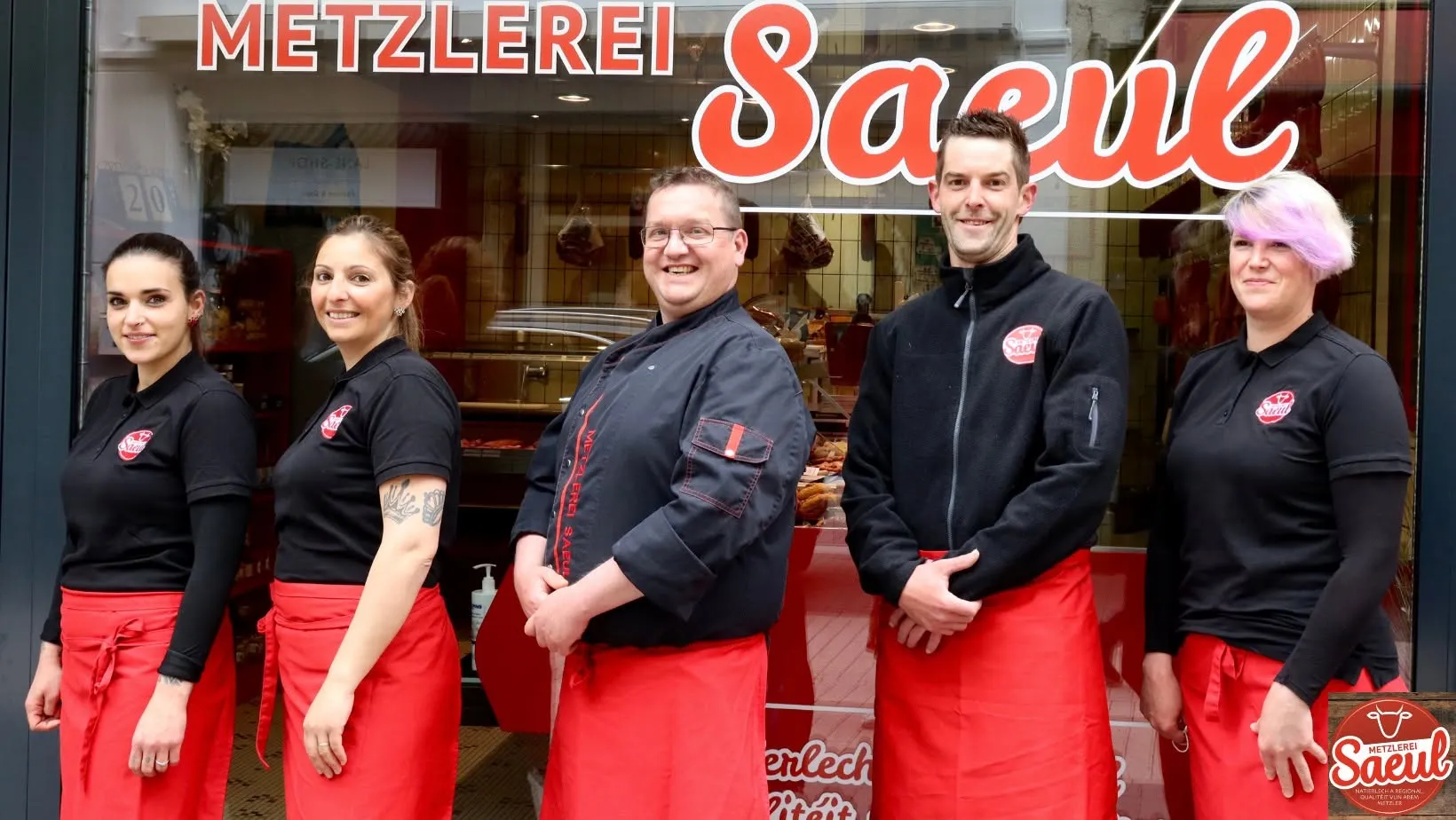 L'équipe de la Metzlerei Lucien Saeul — cinq collaborateurs en tenue noire et rouge Saeul devant la boutique d'Echternach